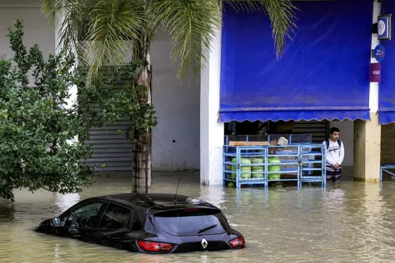 A man stands by cooking gas canisters near a sunken vehicle along an inundated street in Morocco's northwestern city of Ksar el-Kebir on January 29, 2026. / Ph. AFP